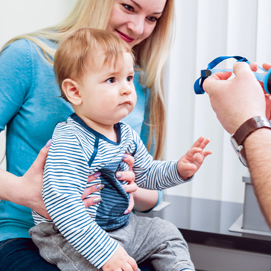 A mother holds her baby while he gets his eyes examined for the first time by an optometrist.