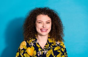 Against a blue background, a young adult in a lemon-print button-up shirt winks to mimic an eye twitch