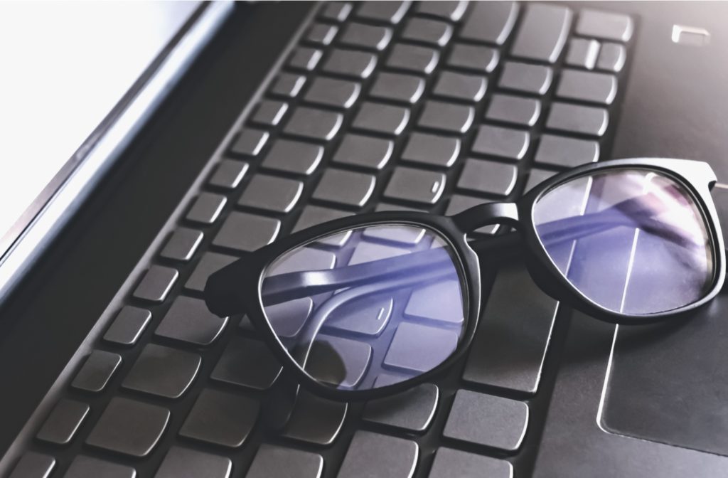 A set of black blue light glasses resting on the black keyboard of a laptop.