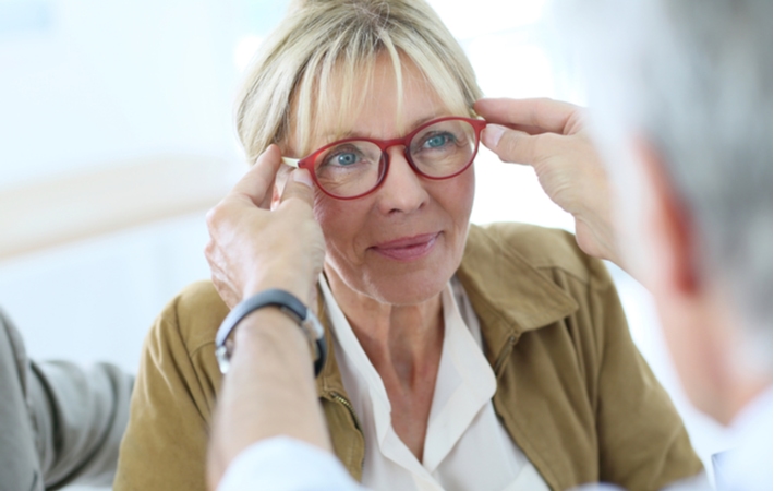 A woman getting fitted for new glasses by an optician who is placing the new glasses on her face