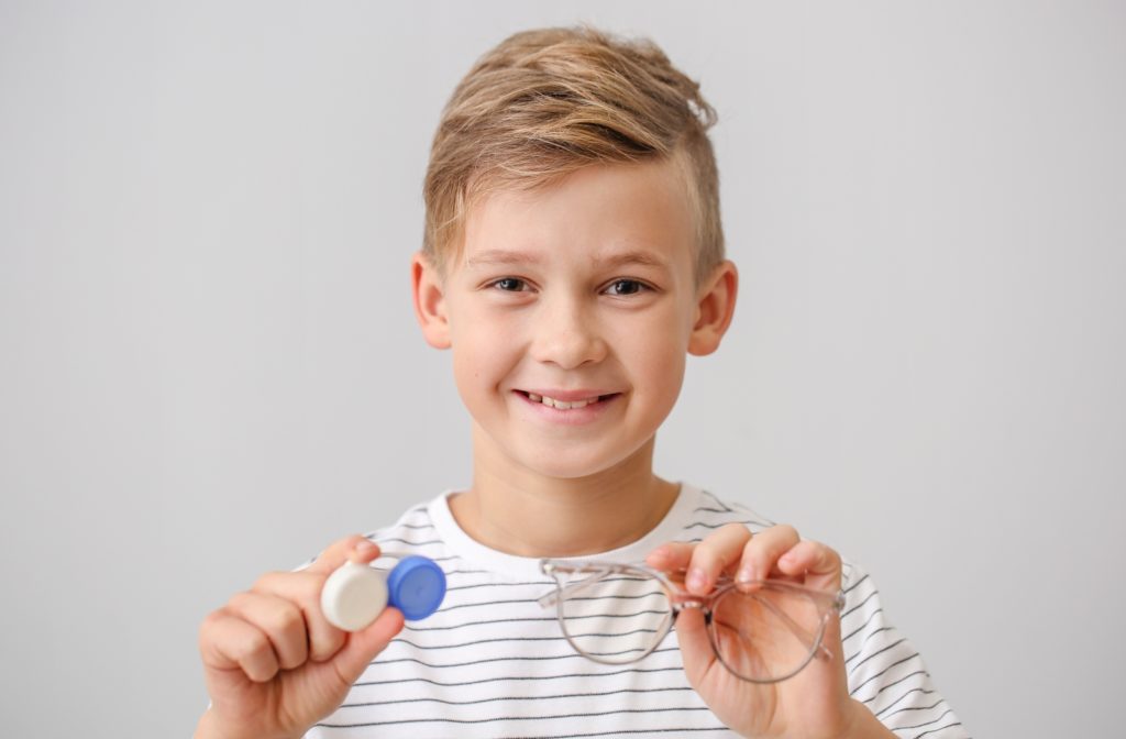 A young boy holding a pair of eyeglasses and contacts to help correct his nearsightedness