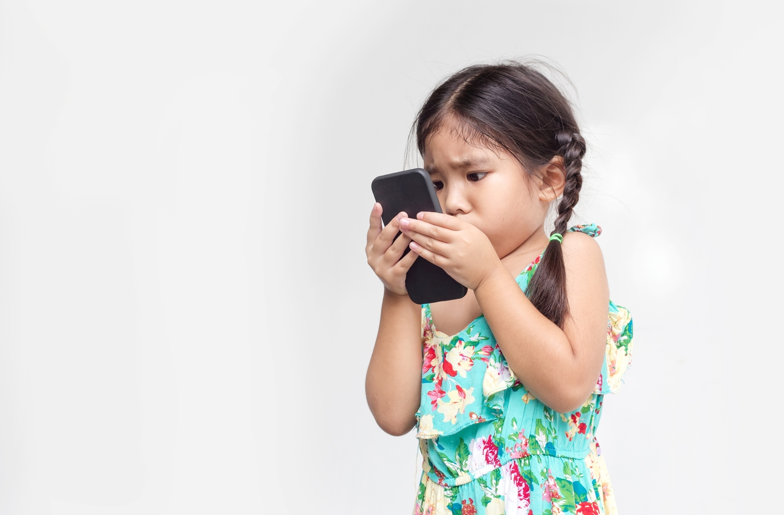 A young girl in front of a white background holding a cell phone extremely close to her face as she is nearsighted due to her myopia