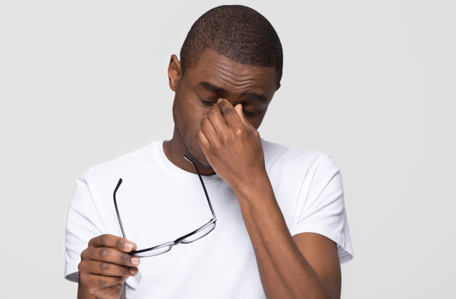 A man taking off his glasses and rubbing his eye due to irritated eyes