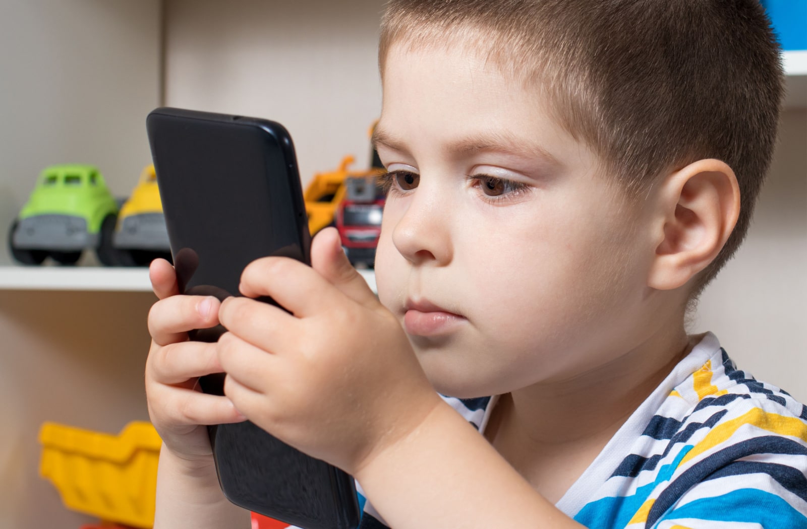 A boy child is holding a smartphone toot close to his face while watching something on the phone screen