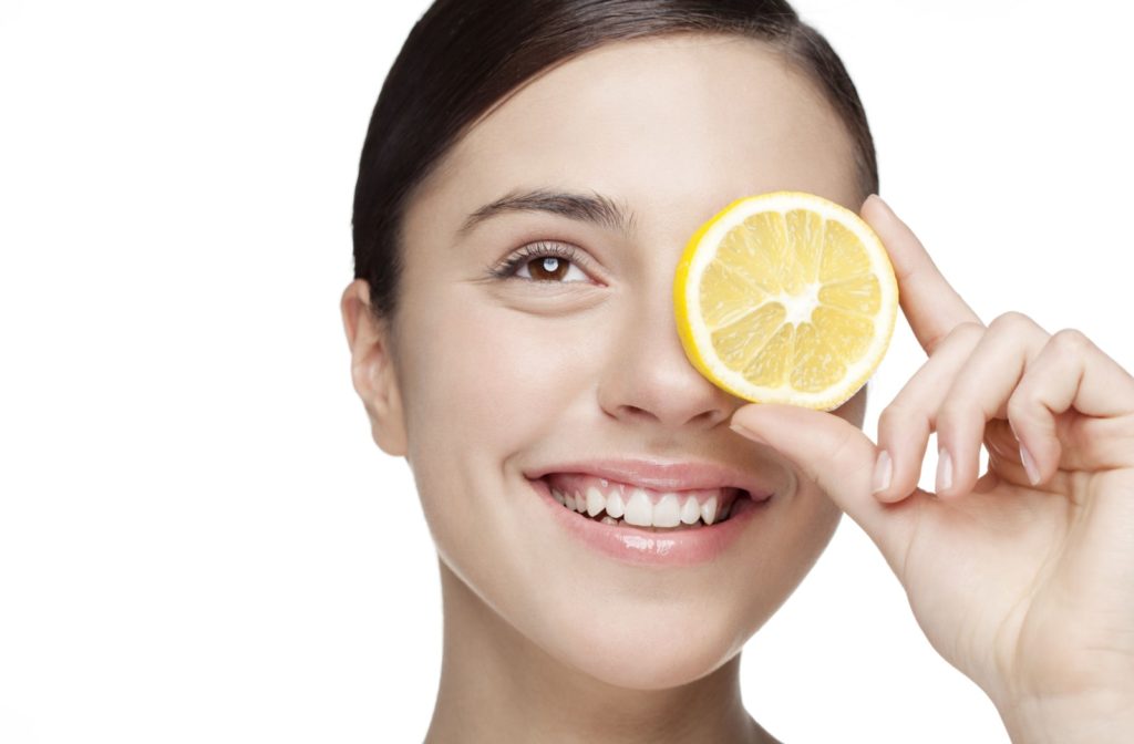 A young woman holding a lemon slice in front of her eye. Lemon and other citrus fruits are good sources of vitamin C with is good for the eye.