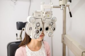 A woman sitting behind a phoropter at the optometrist's office.