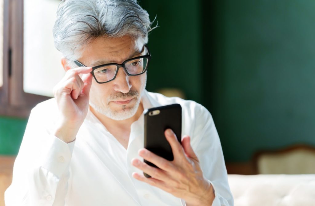 A middle-aged man wearing glasses reads off his phone.