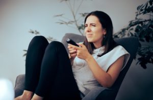 A young woman sitting with a remote control squinting to see the television due to myopia.