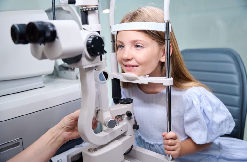 A young girl smiling while an out-of-frame optometrist checks their eyes during an eye exam.