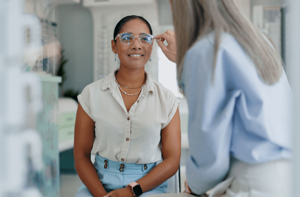 An optician assists a young adult in trying prescription glasses on.