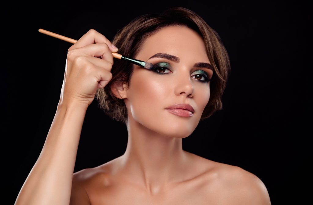 A portrait of a beautiful woman applying makeup to her eyes with a makeup brush.