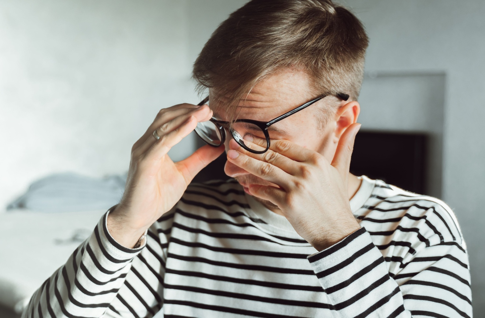 A man in a striped shirt rubbing eyes under glasses.