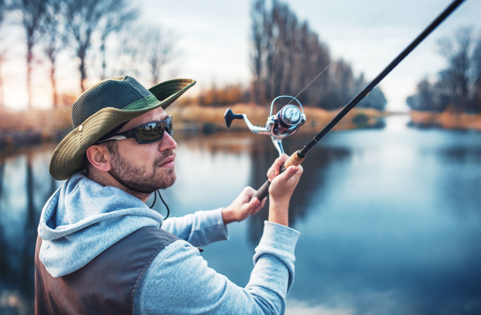 A person fishing on a lake wearing polarized sunglasses to cut down on the glare of the water.