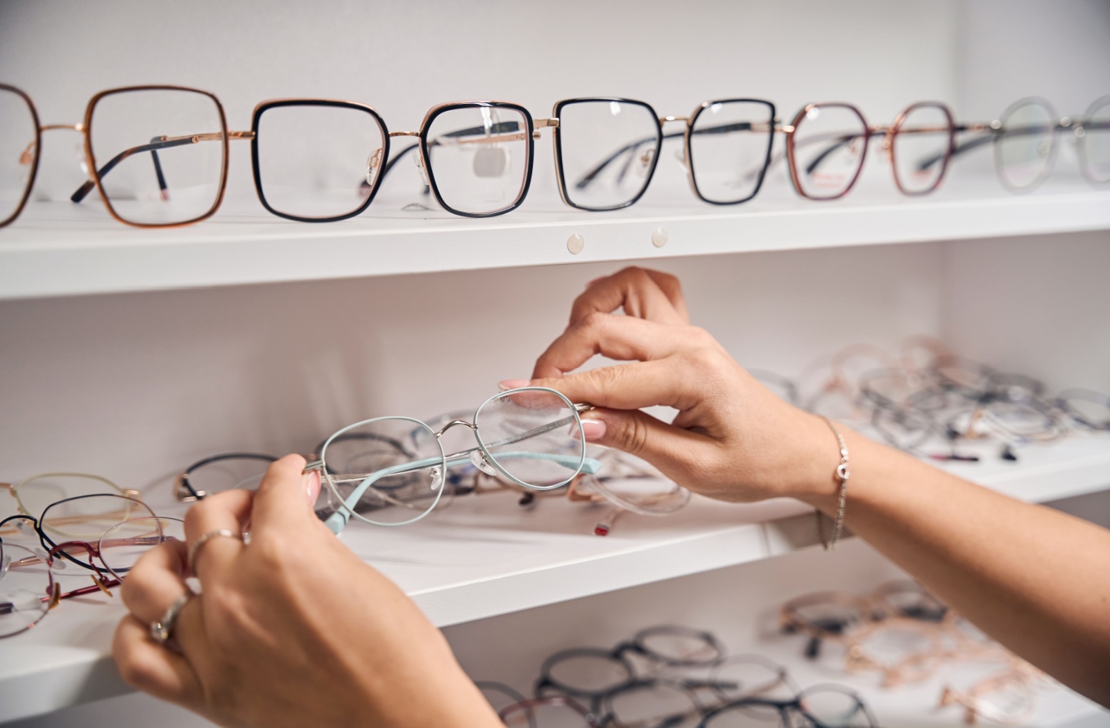 A close up photo of hands selecting glasses from a display shelf.