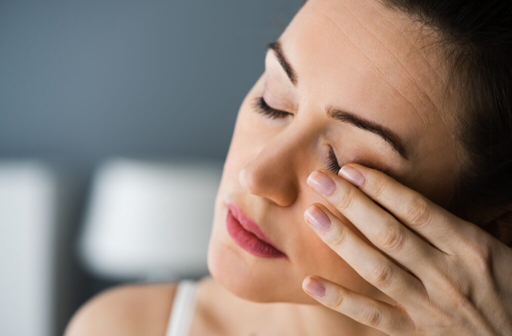 Close-up of a person gently touching their eye with a look of discomfort, suggesting the sensation of something in the eye.