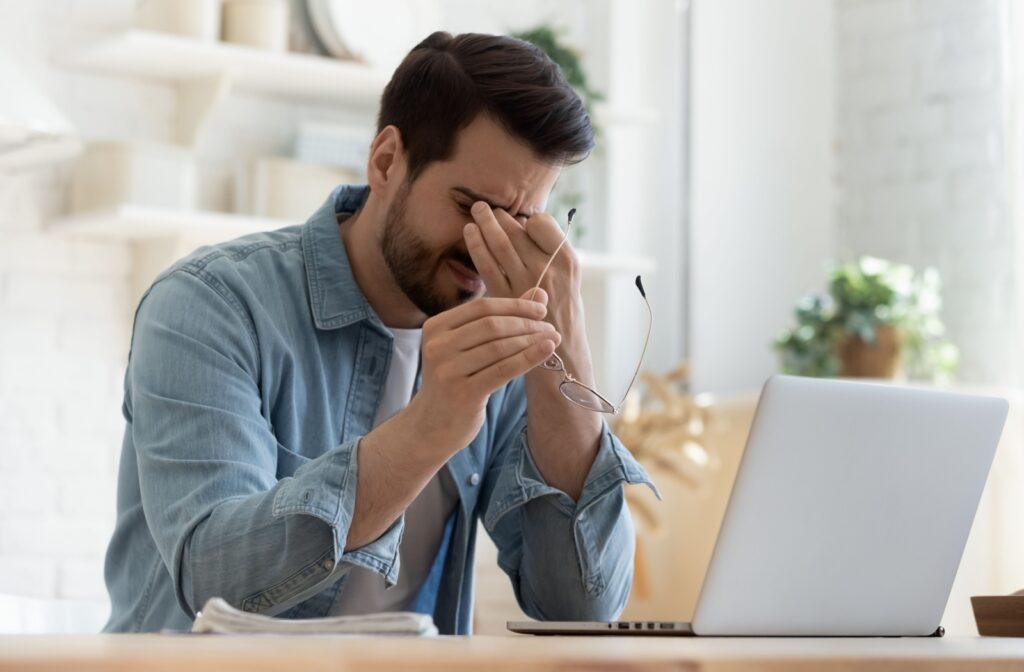Person sitting in front of a computer, pressing fingers between their eyes, indicating discomfort due to dry eye.