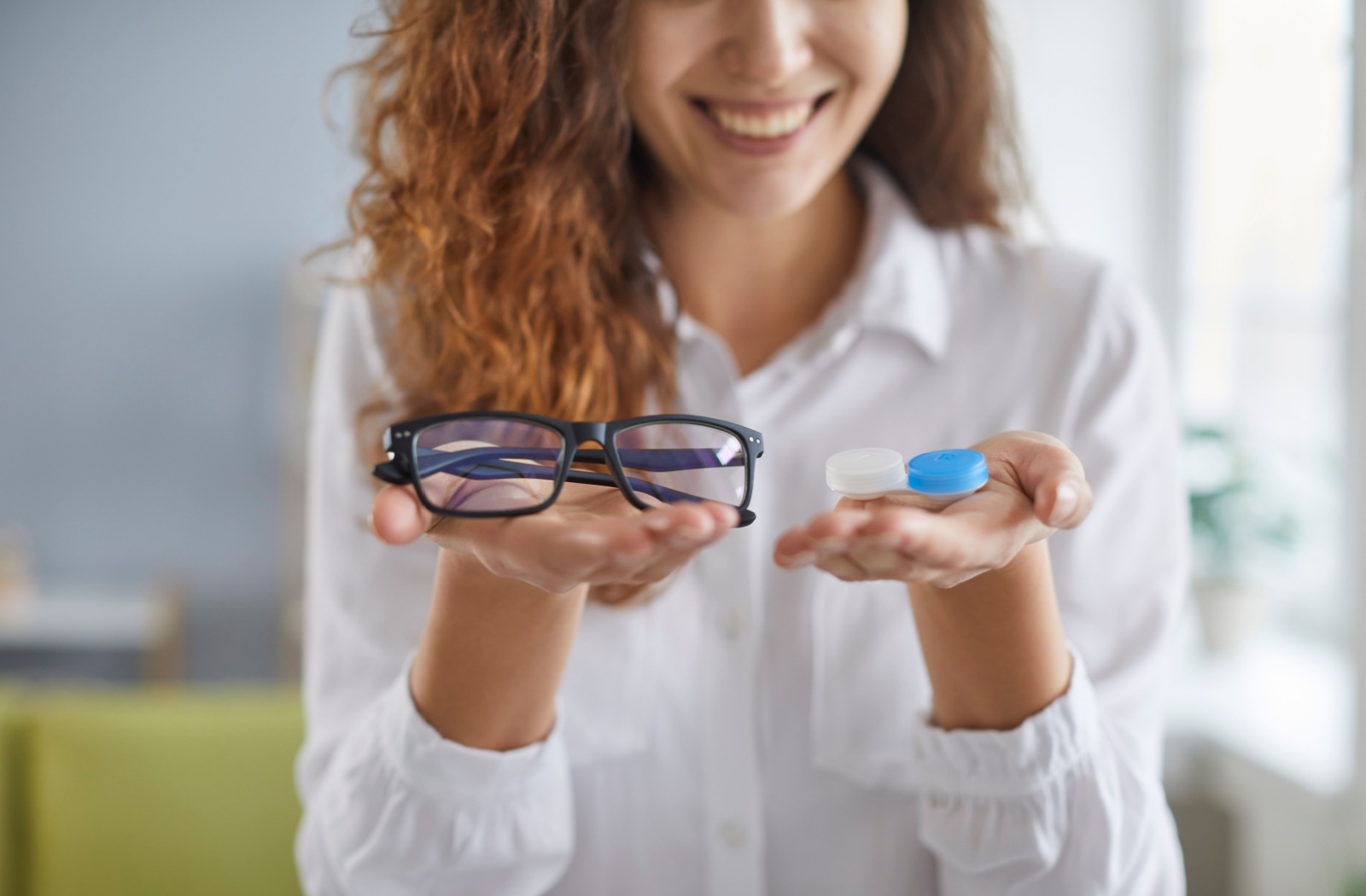 A person looks at the glasses they hold in one hand and the contact lens case they hold in their other hand