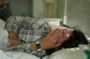 A person rubs their eyes as they are laying in bed just waking up