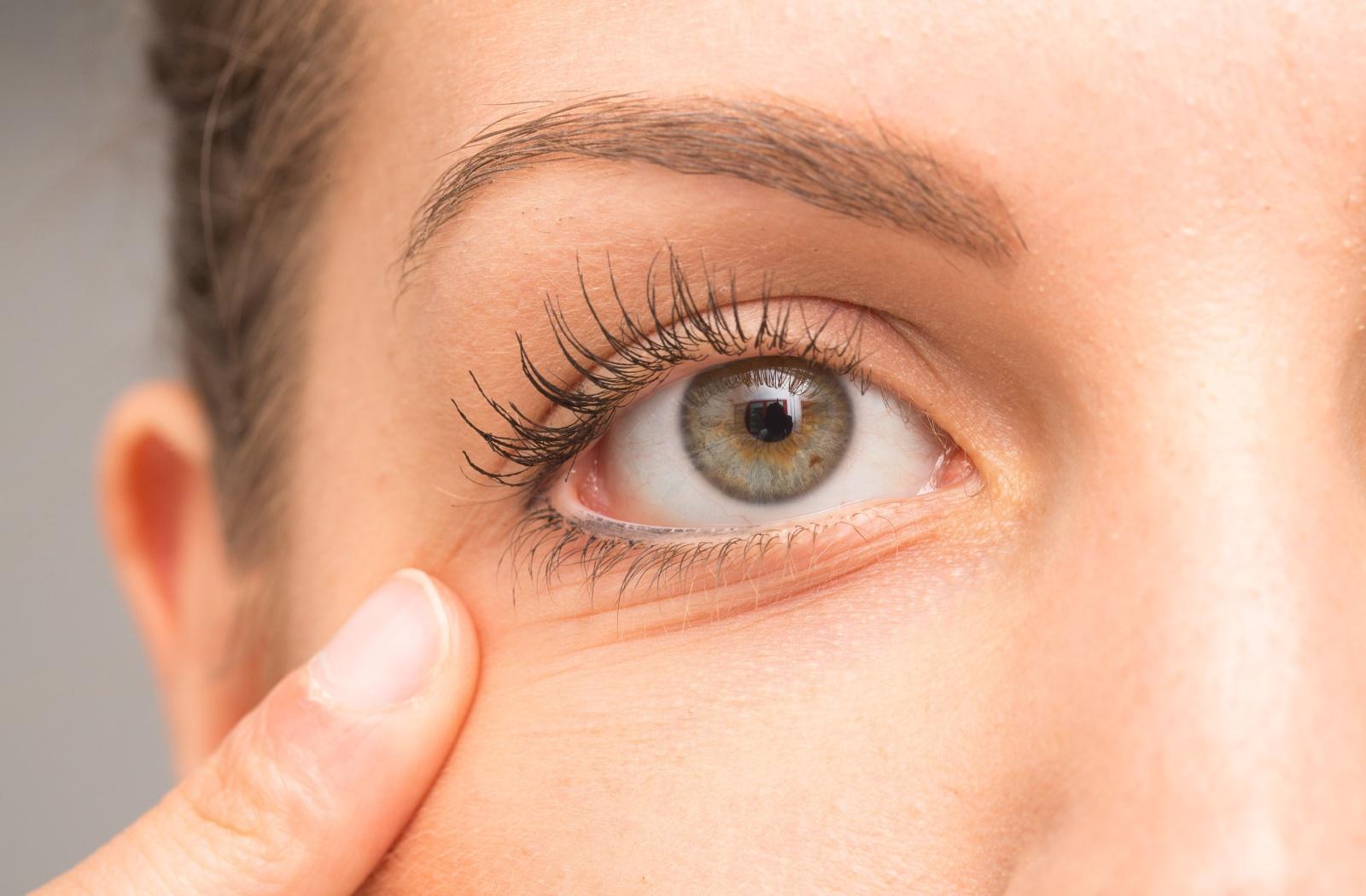 A person pulling on their skin under their eye to show their eye more fully