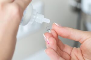 a person applying some contact lens solution to their contact lens that is being held in their hand.